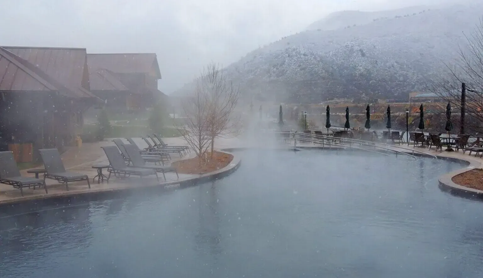 Foggy outdoor pool with steaming water beside lounge chairs and mountains in the background