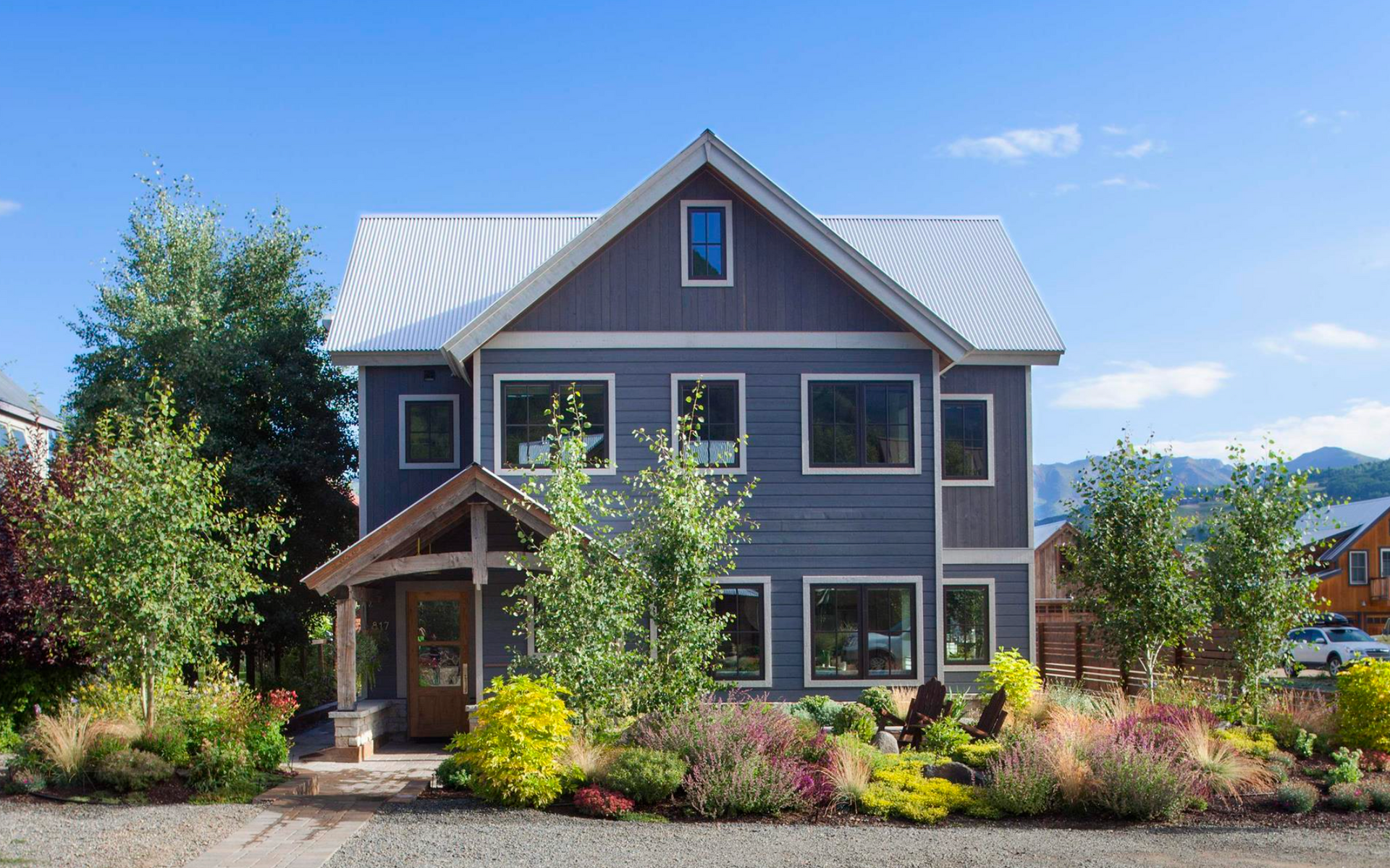 Two-story gray house with white trim, a front porch, and landscaped yard under a bright blue sky