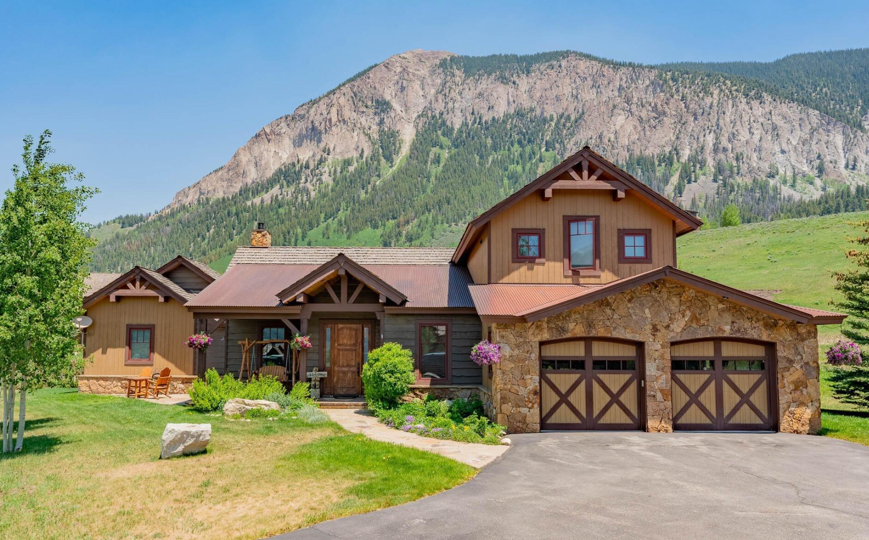 Rustic mountain home with stone garage, green lawn, and rocky hillside backdrop