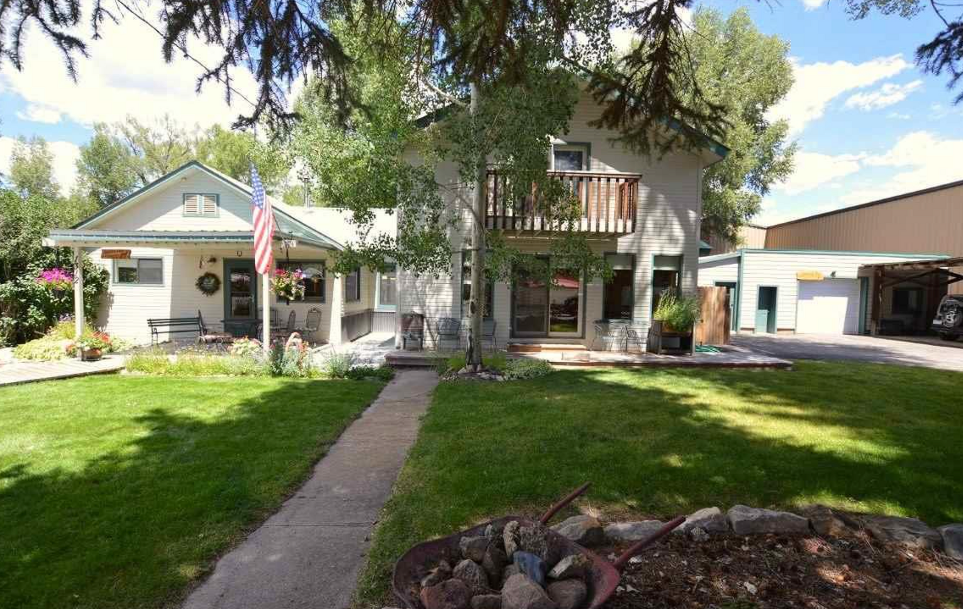 Suburban house with a front lawn, walkway, American flag, and trees in bright daylight