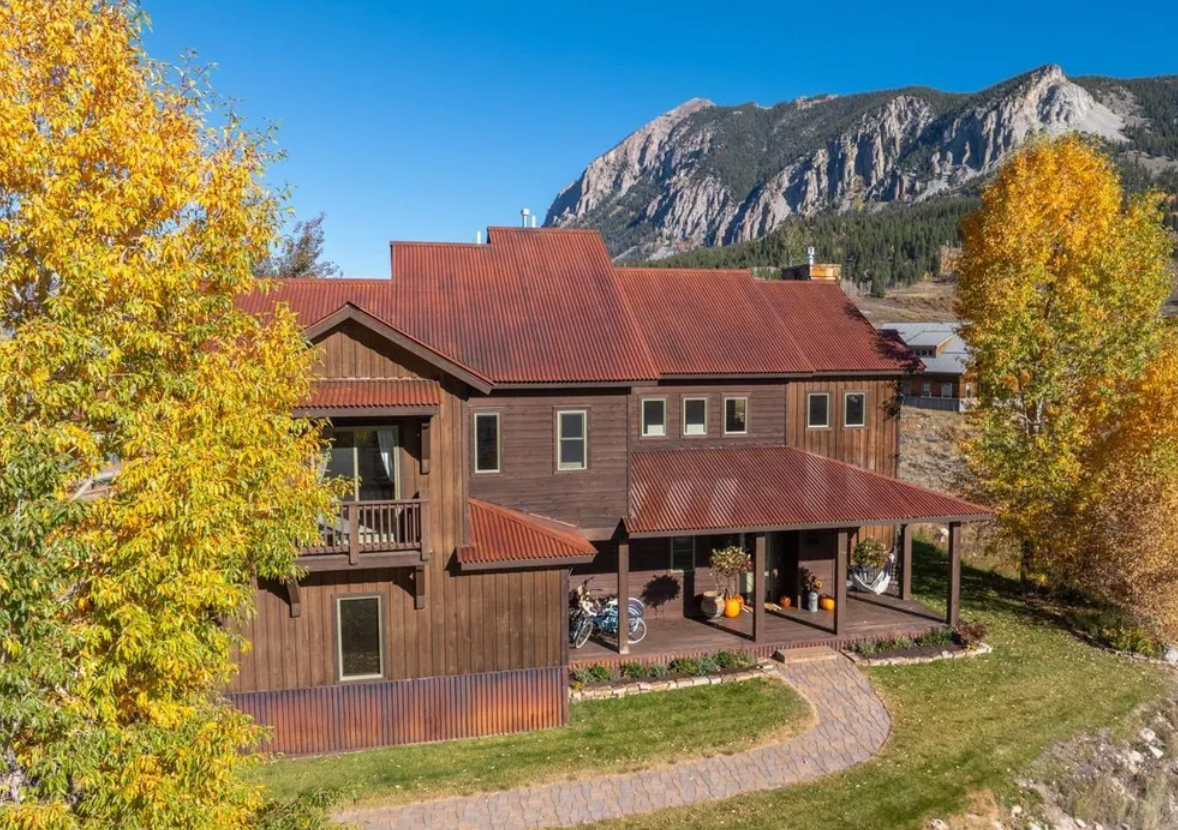 Rustic red-roofed house with autumn trees and mountains in the background