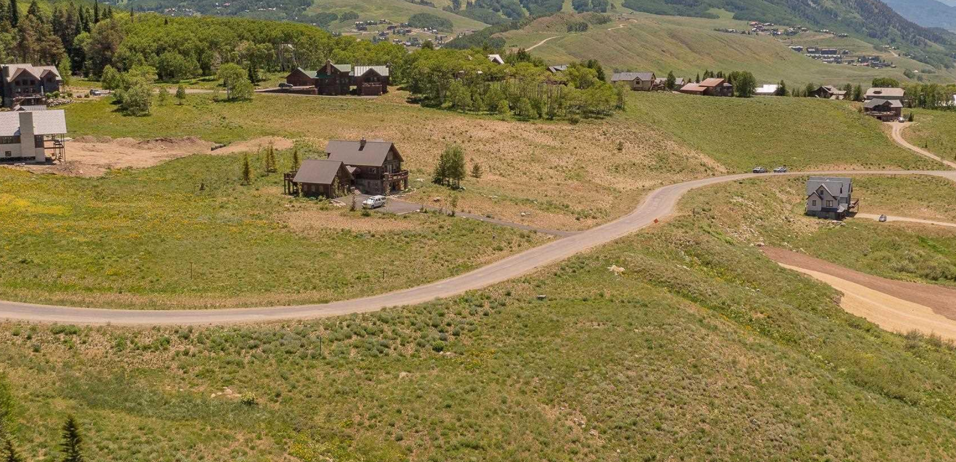 Wide grassy hillside with a winding dirt road and scattered small houses under a clear sky
