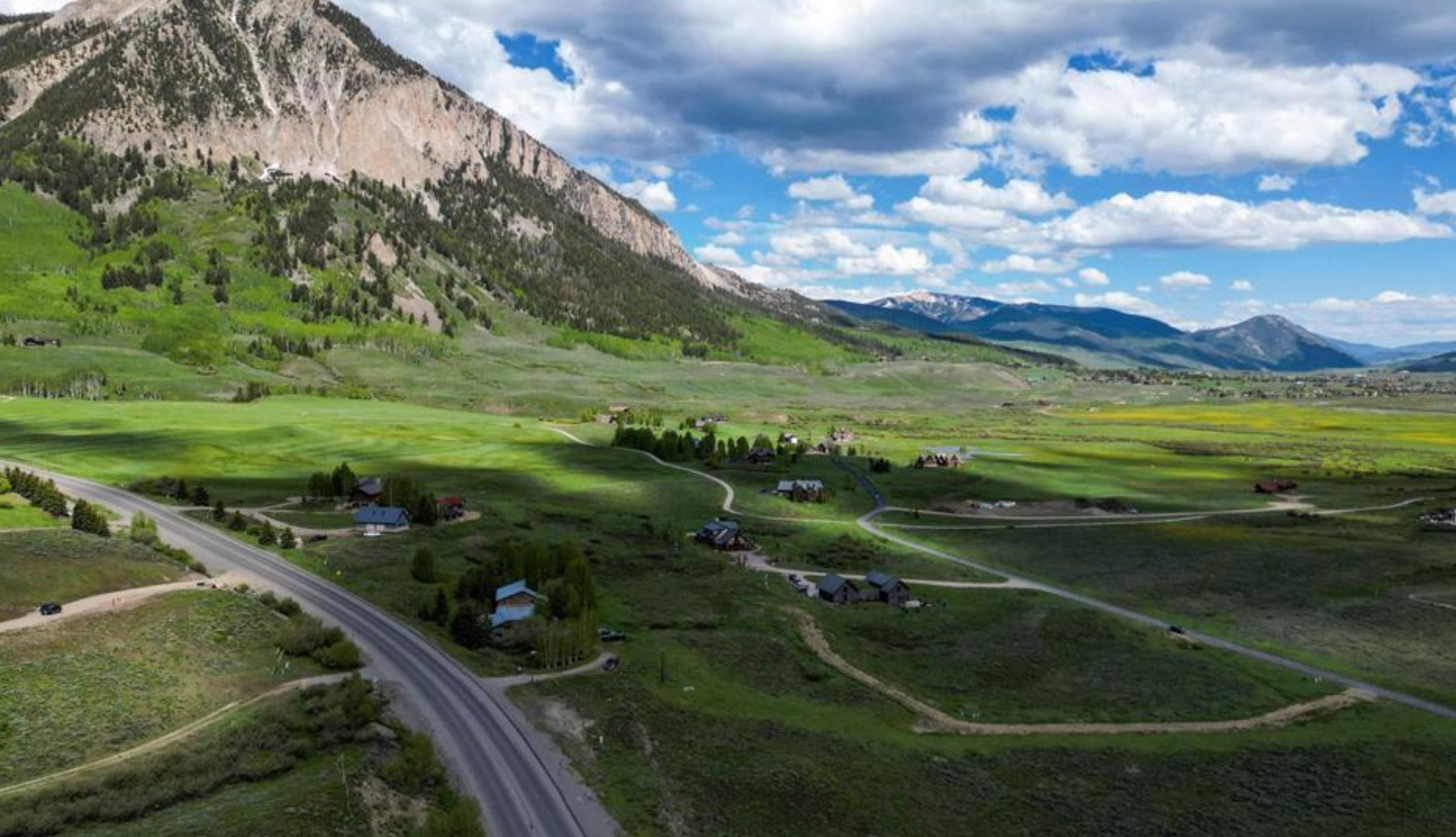 Winding road through green valley beneath rocky mountains and cloudy blue sky