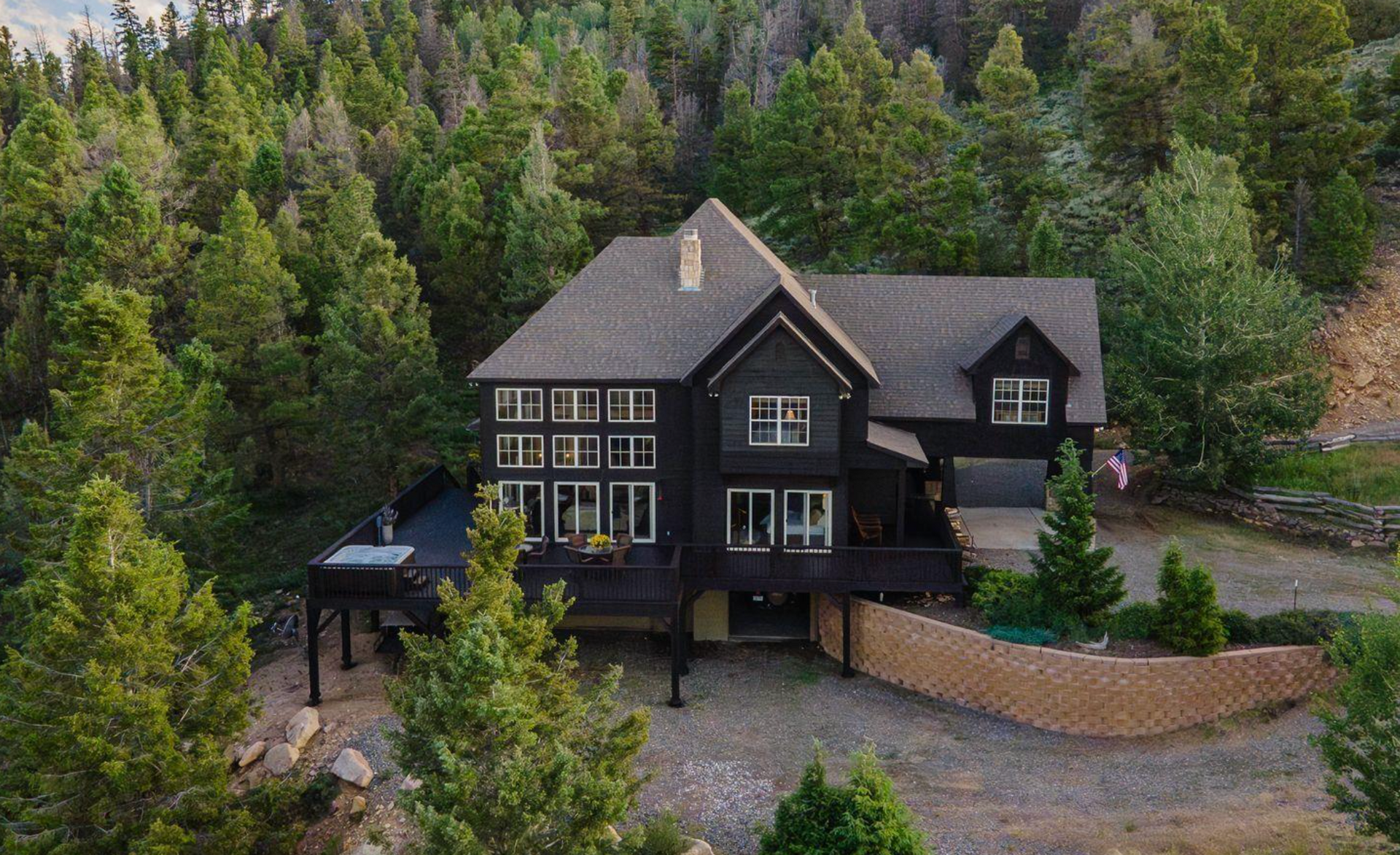 Dark modern house with steep roof nestled in dense green forest hillside