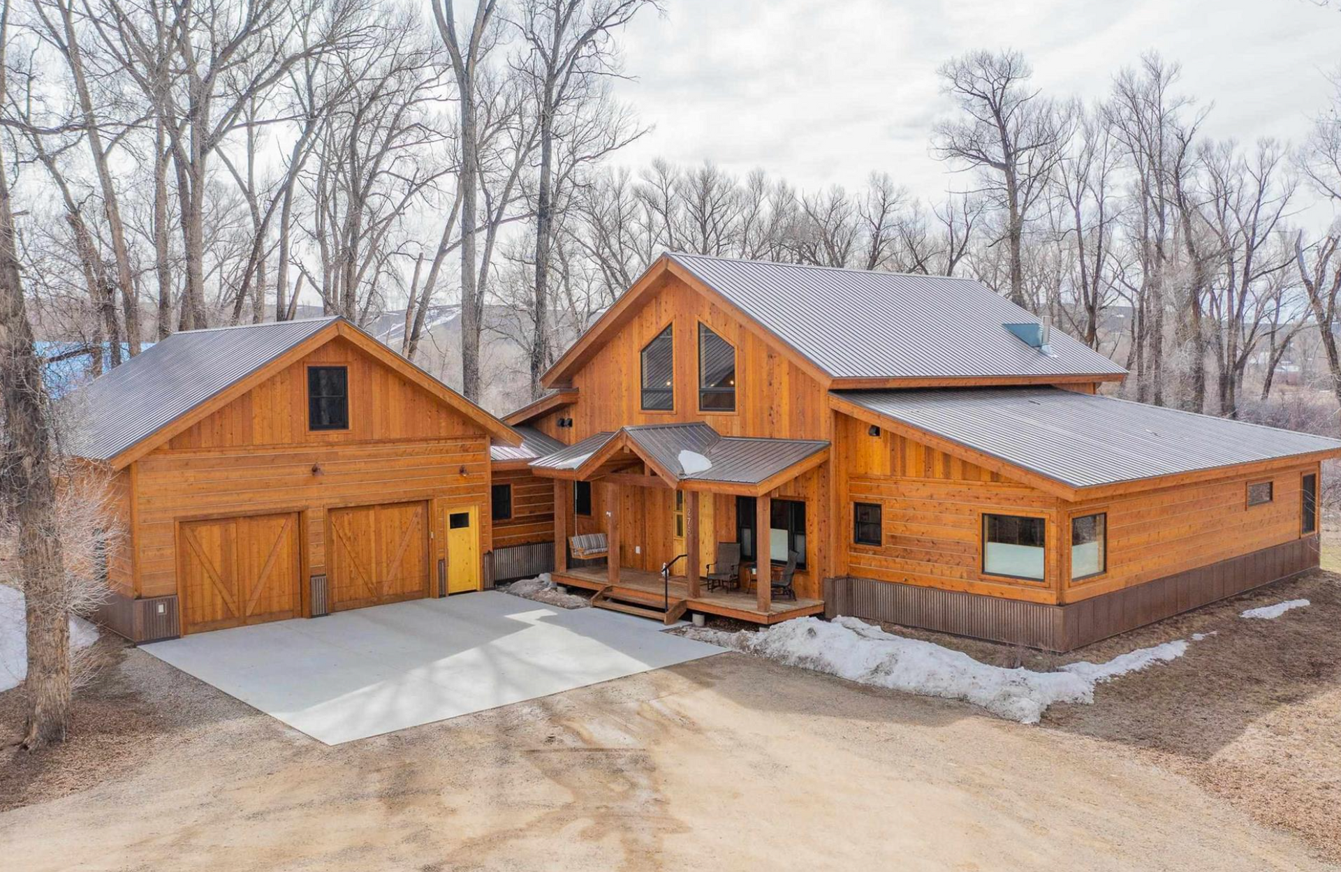 Wooden cabin-style house and detached garage with metal roofs in a wooded setting