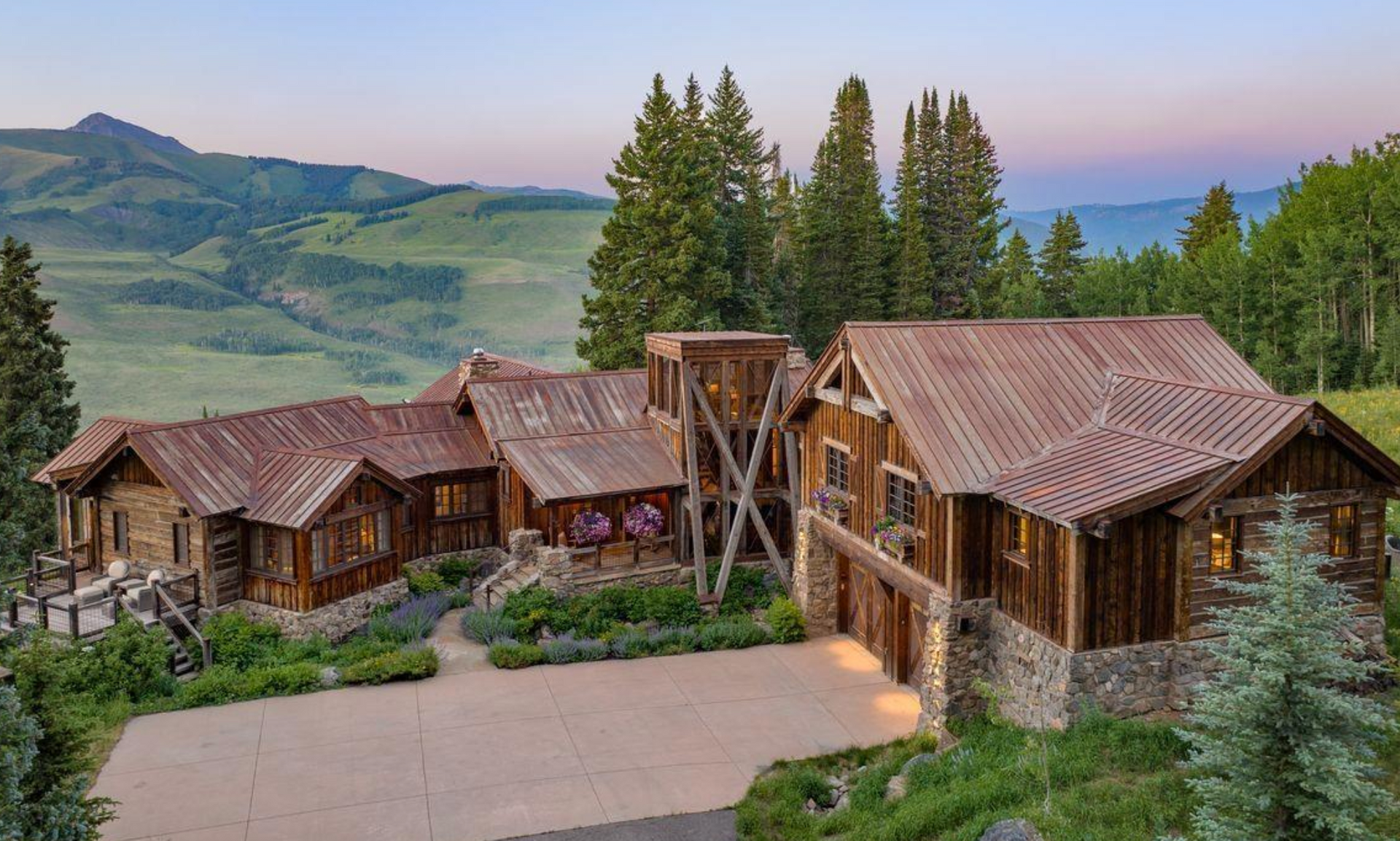 Rustic wooden cabins with red roofs on a hillside, overlooking green mountains at dusk