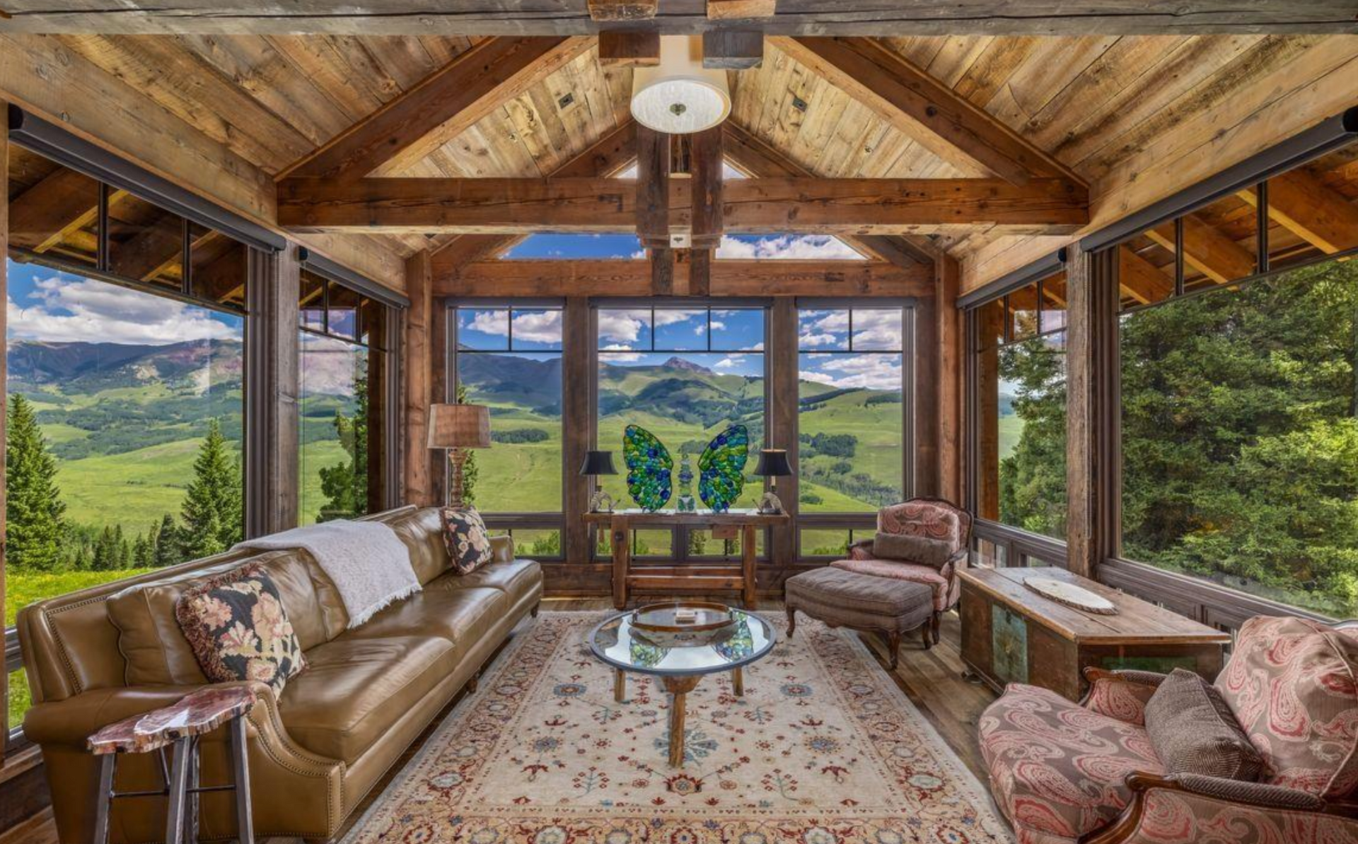 Rustic covered patio lounge with leather sofas, wood beams, and mountain lake views