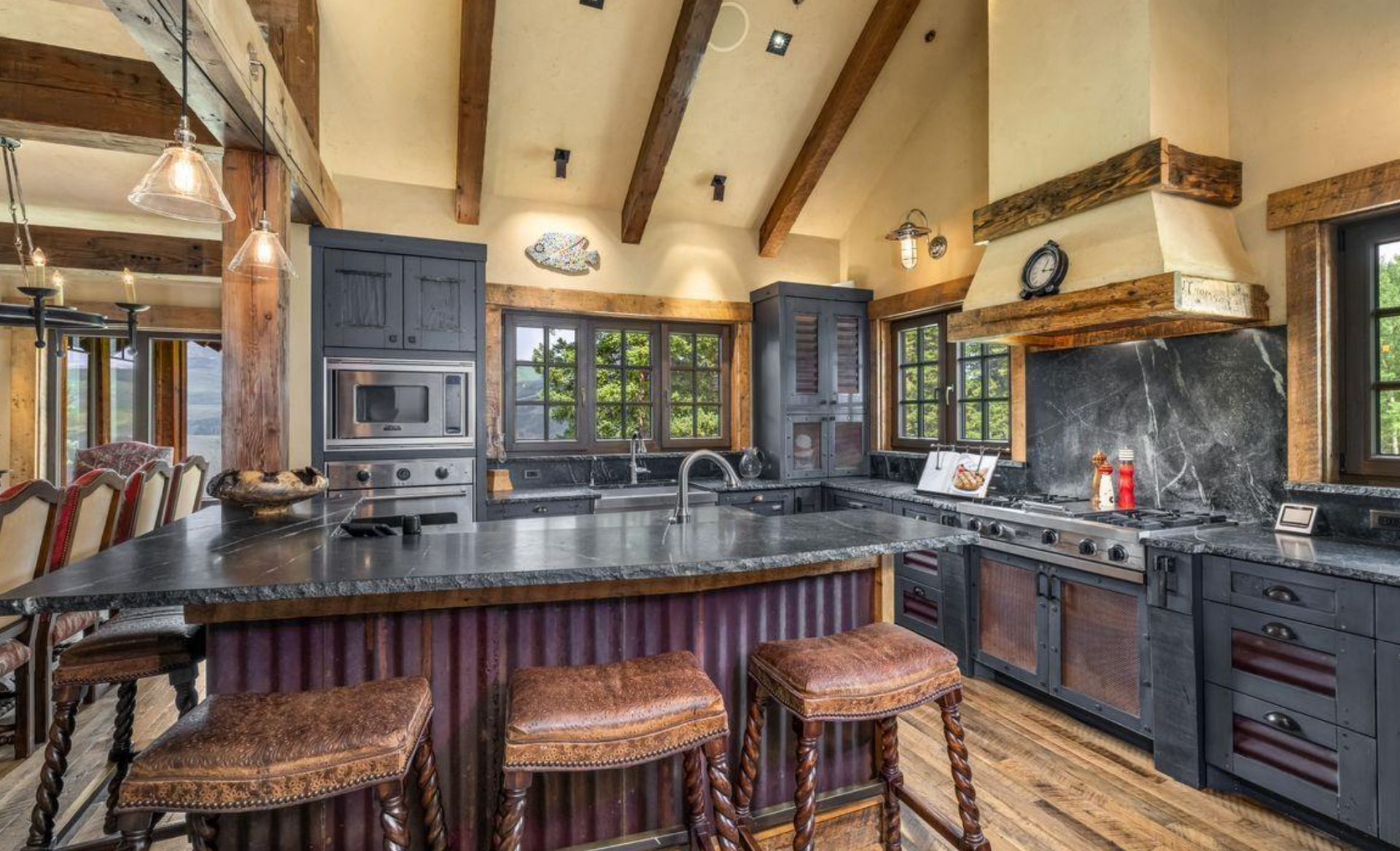 Rustic kitchen with dark cabinets, wood beams, stone walls, and a large island with stools