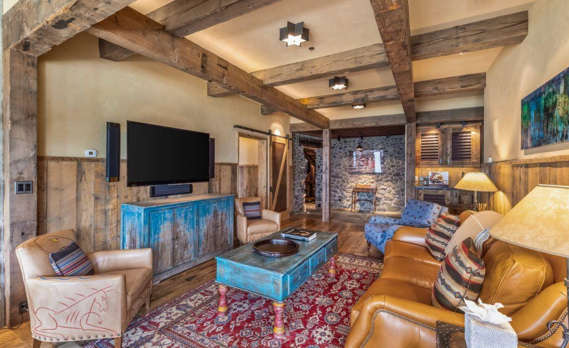 Cozy rustic living room with tan leather sofa, blue coffee table, wall TV, and stone fireplace