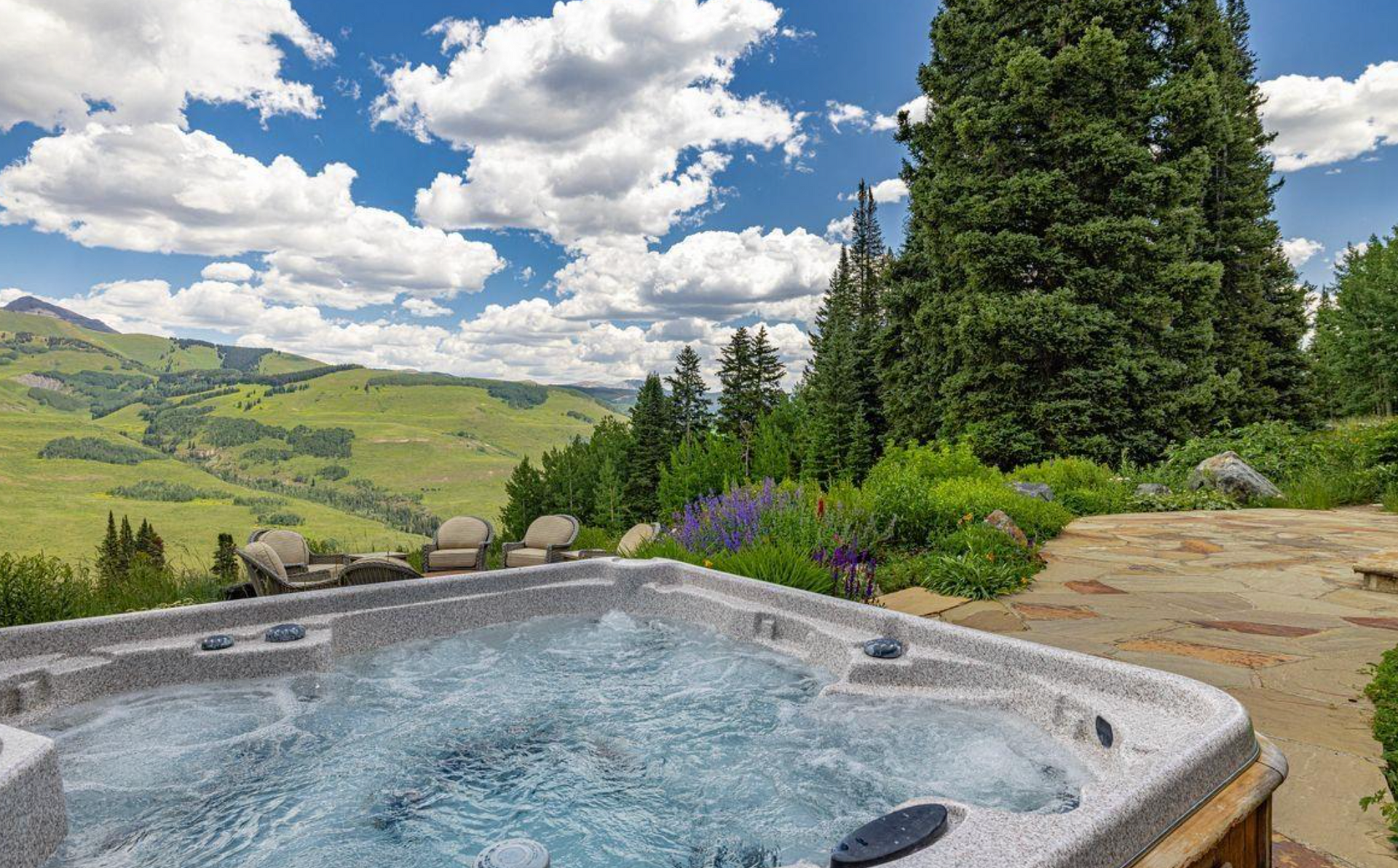 Hot tub with bubbling water overlooking a green valley, mountains, and cloudy blue sky