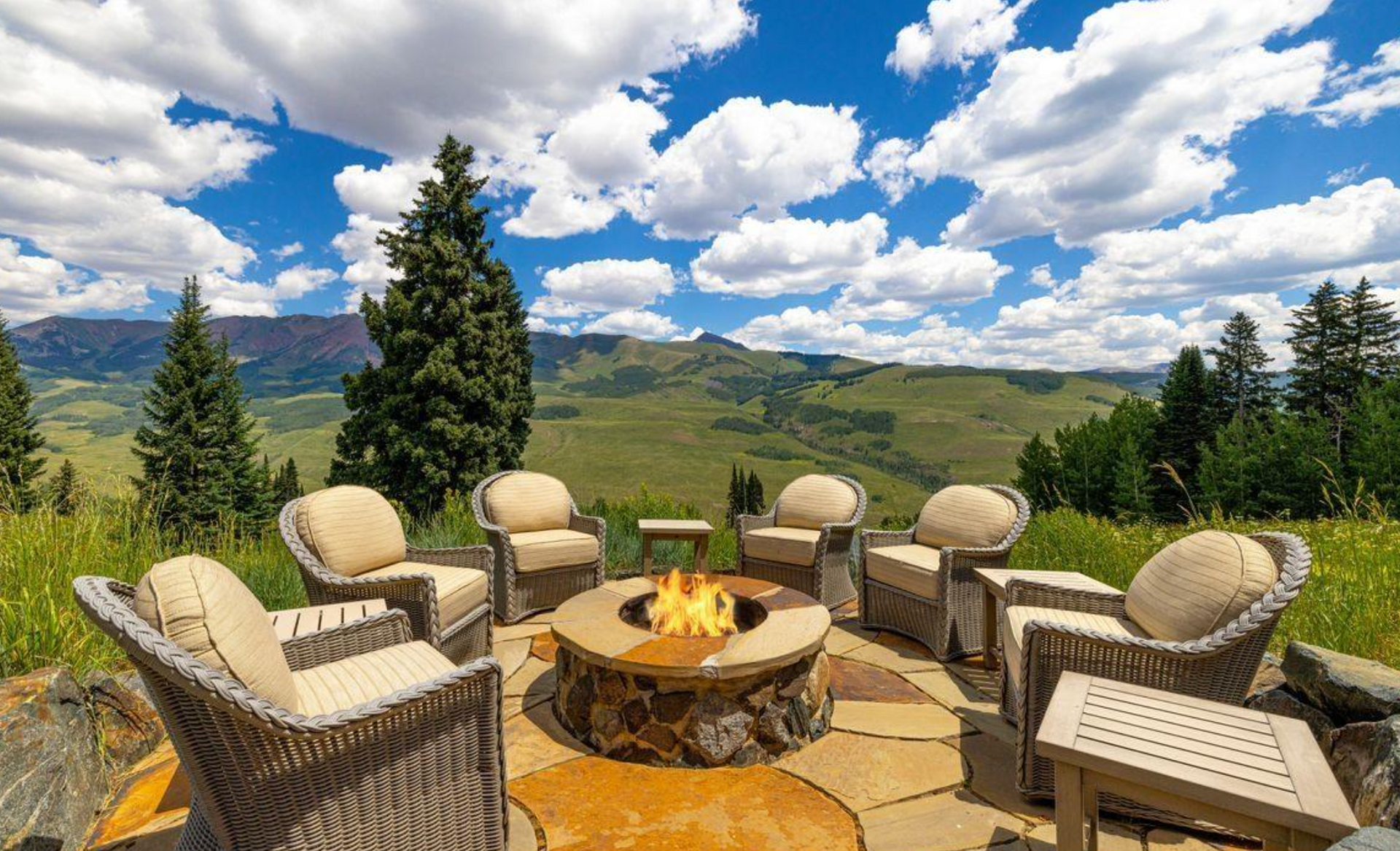 Patio seating around a fire pit overlooking green hills under a cloudy blue sky