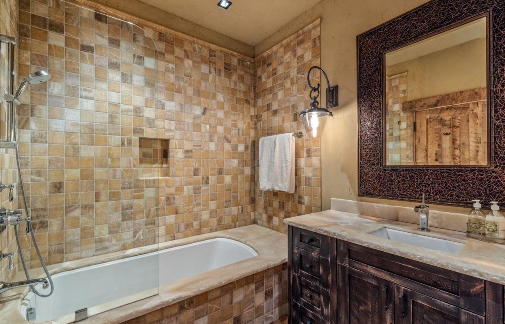 Tiled bathroom with a bathtub, dark vanity, and large mirror under warm lighting