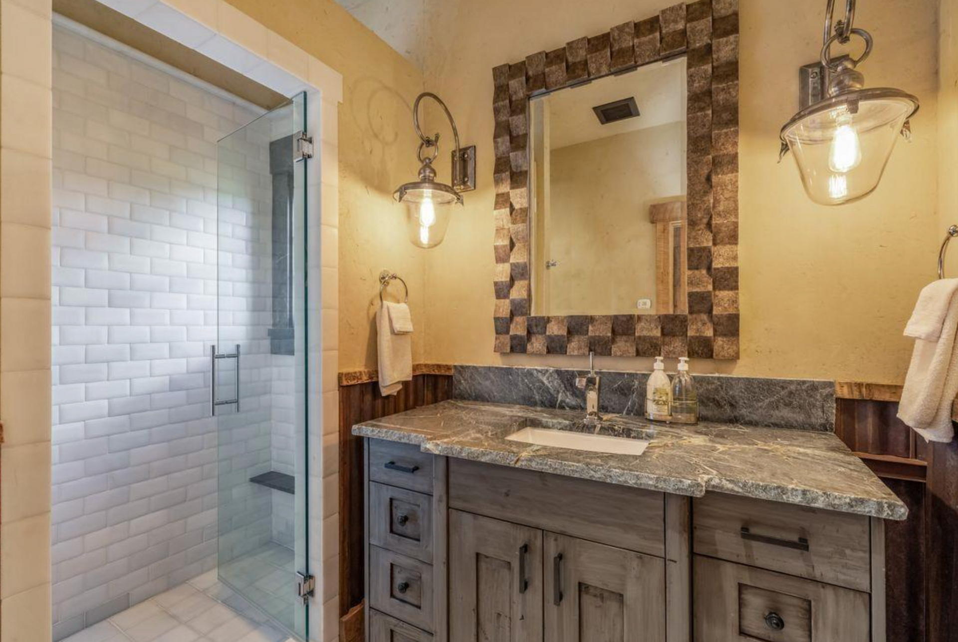 Bathroom vanity with granite countertop, mirror, sconces, and glass shower enclosure