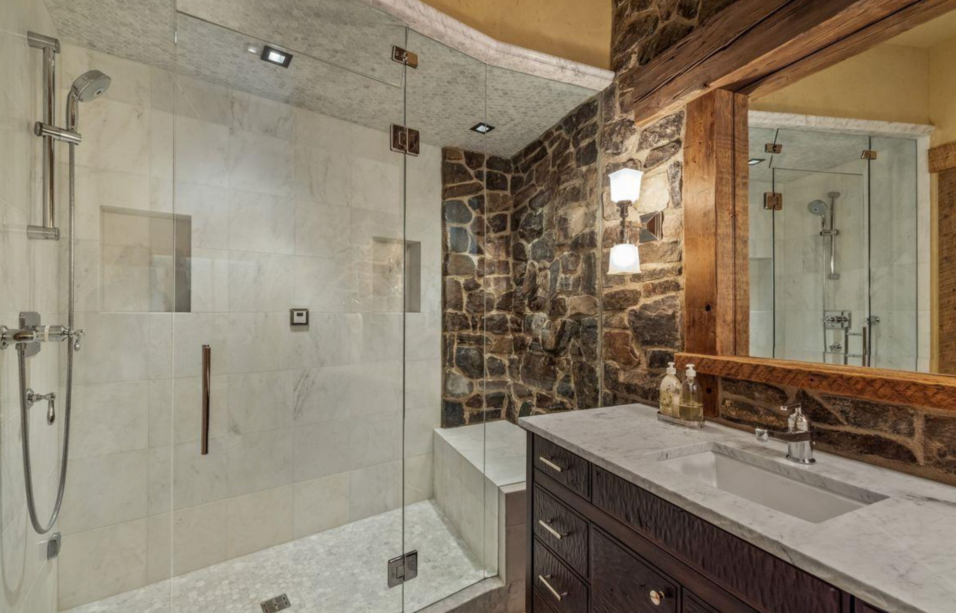 Modern bathroom with glass shower, stone accent wall, and dark wood vanity with large mirror