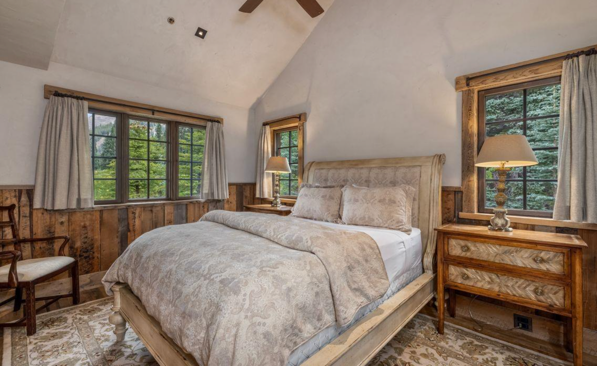 Cozy bedroom with a large bed, wood-paneled walls, and windows overlooking trees