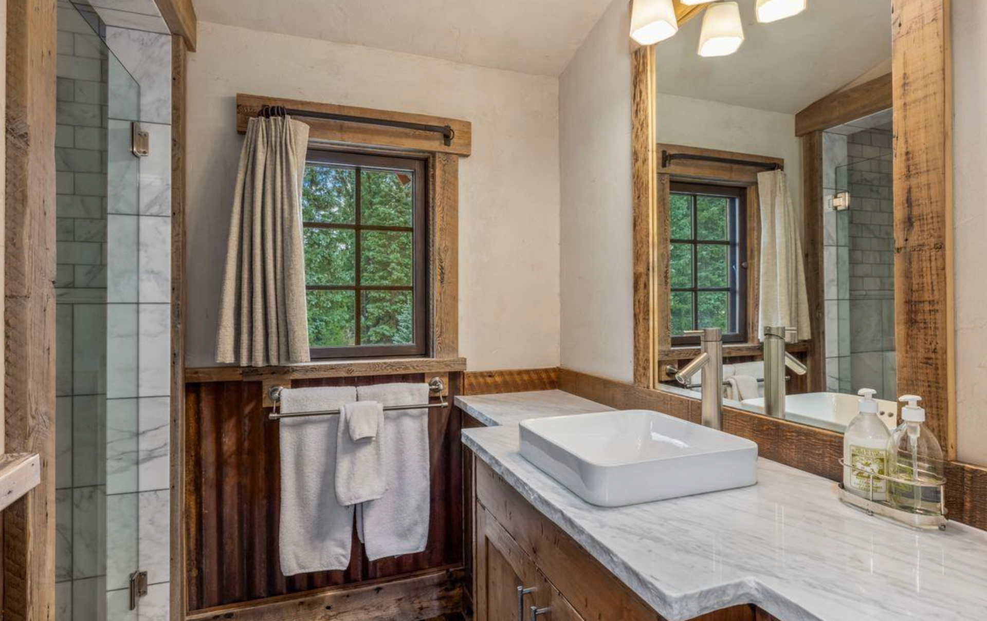Bathroom with marble vanity, sink, mirror, window, and towels above wood-paneled walls