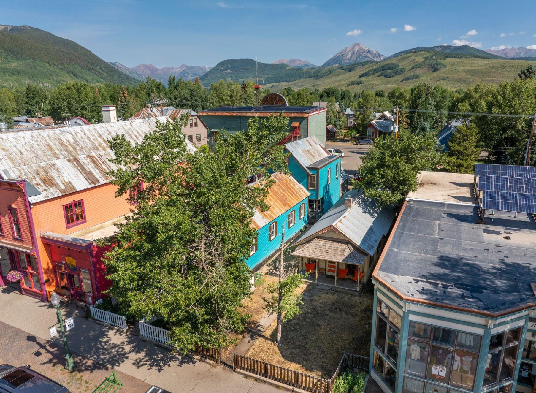 Colorful old-town buildings among trees, with green mountains under a clear blue sky
