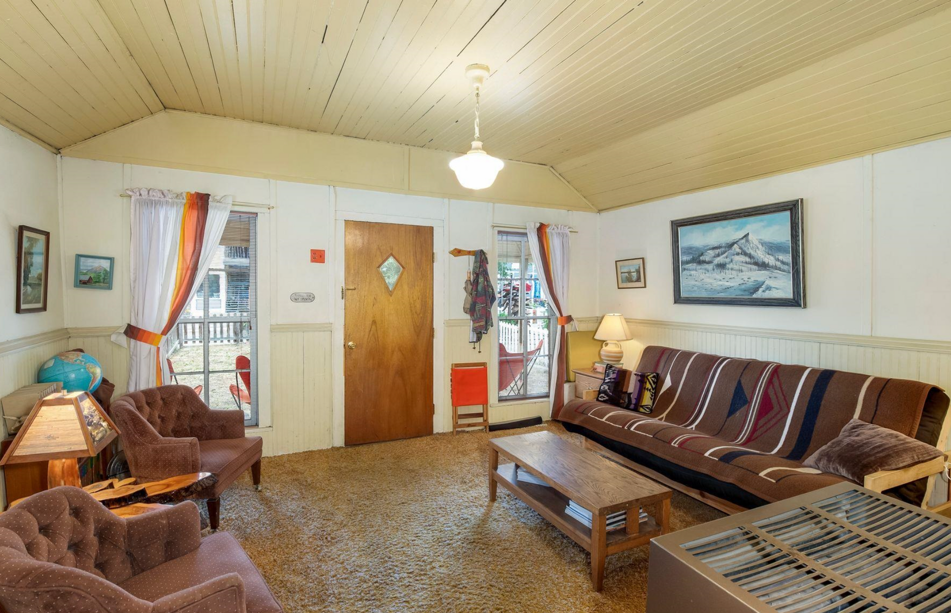 Cozy living room with brown sofa, armchairs, coffee table, wood ceiling, and front door centered between windows.