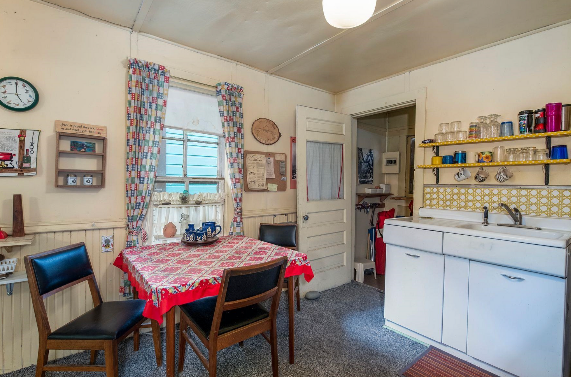 Small kitchen with a red-checkered tablecloth, white cabinets, window, and shelves along the wall.