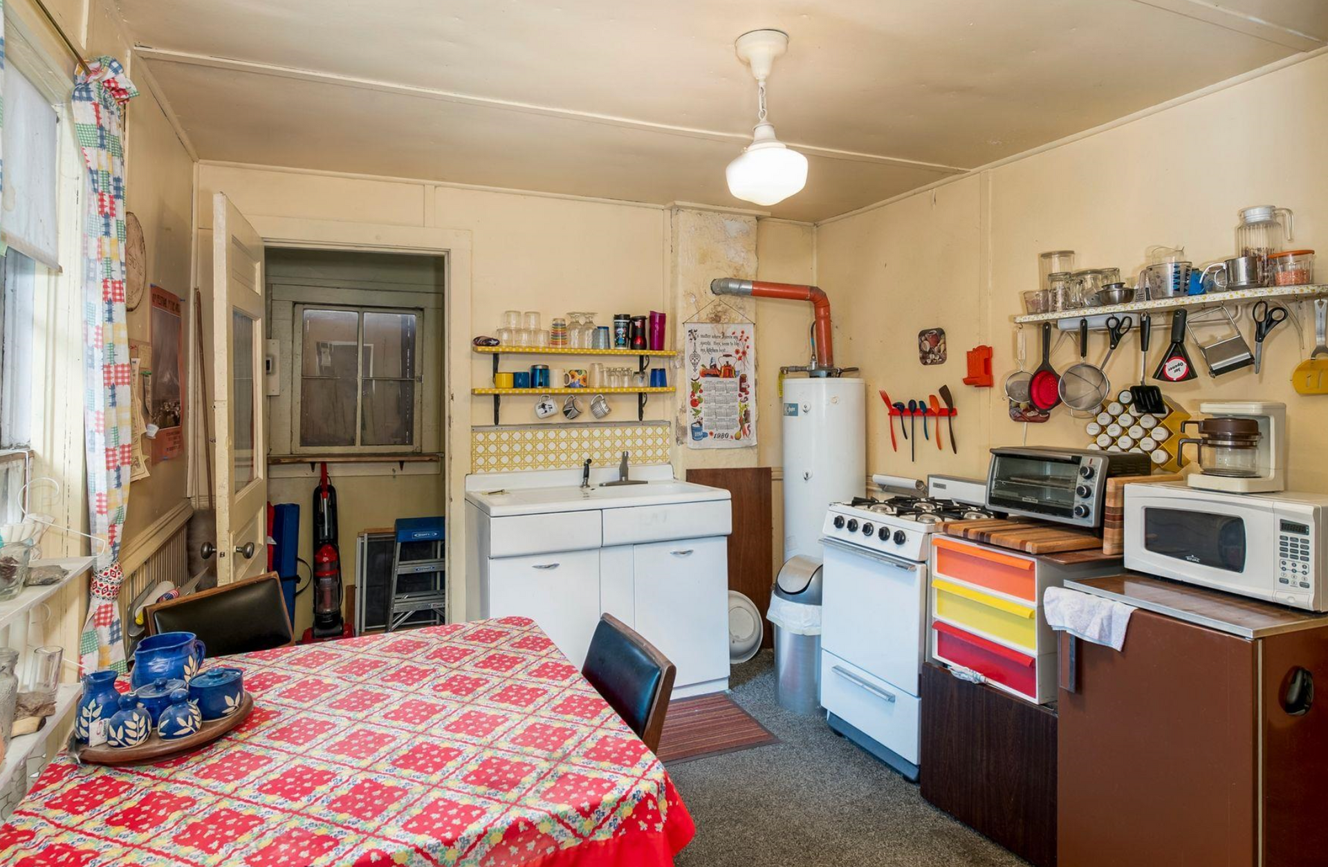 Small kitchen with table, stove, fridge, shelves, and colorful curtains in a modest home
