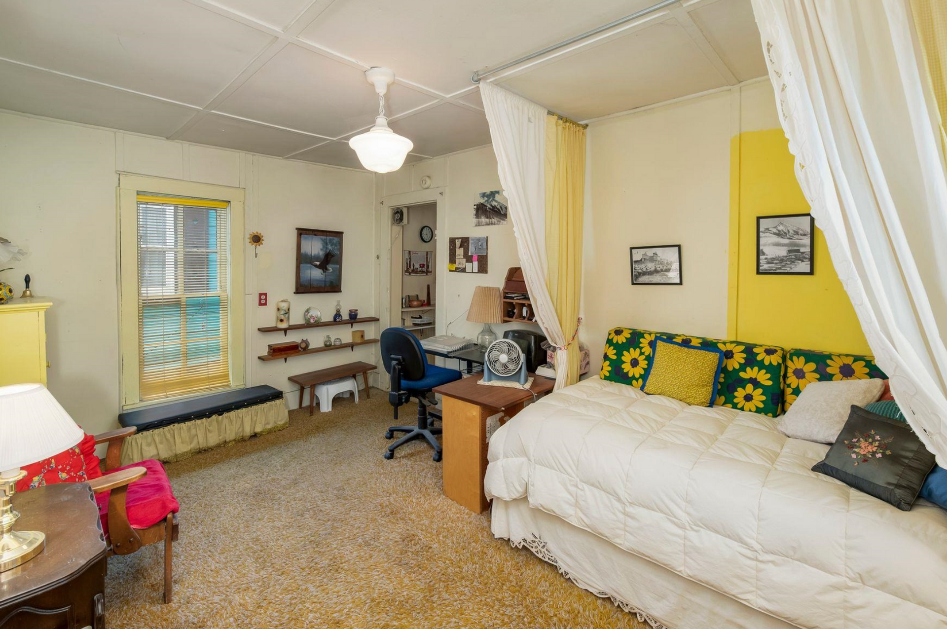 Cozy bedroom with a bed, desk, yellow accent wall, and white curtains