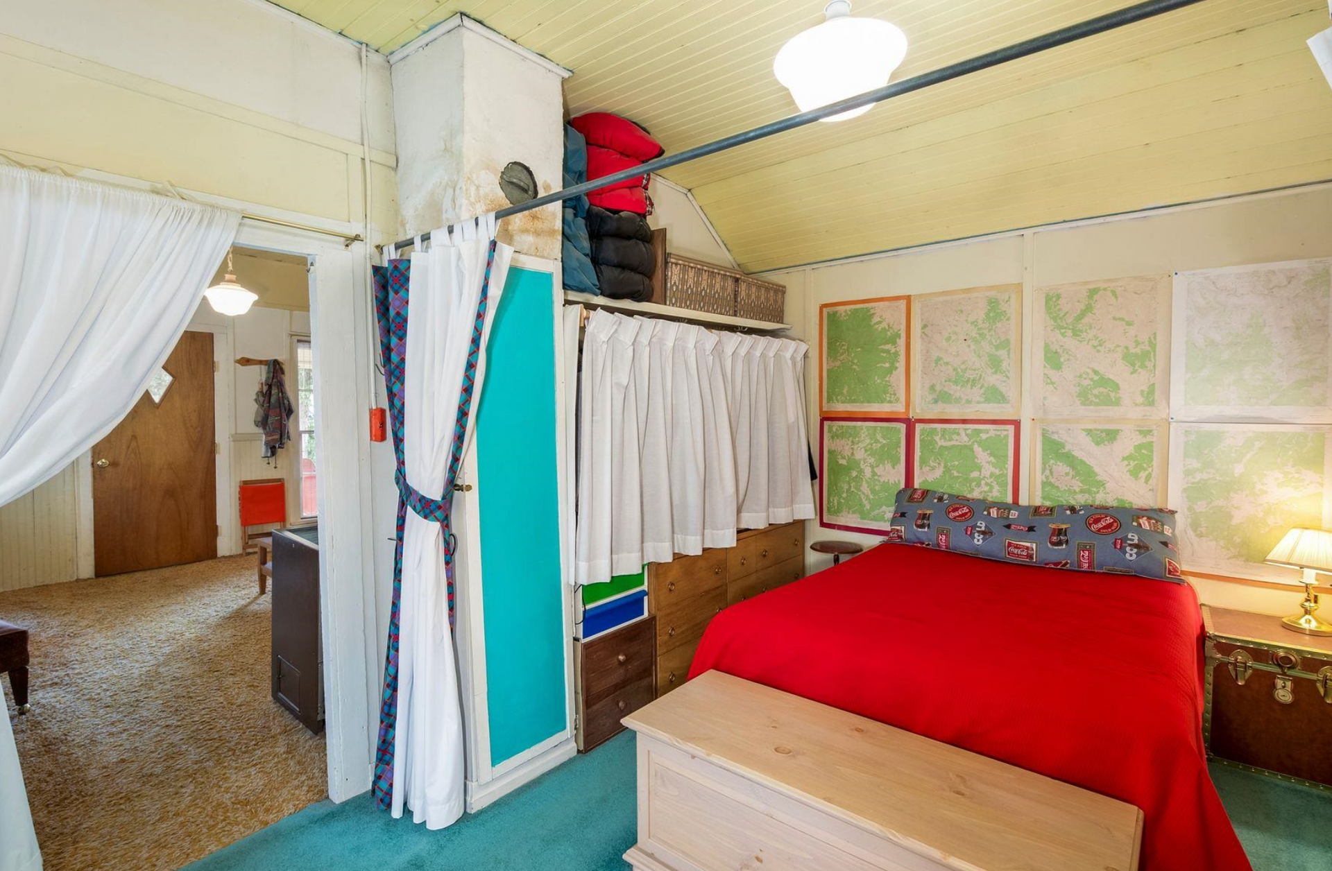 Cozy bedroom with red bedspread, canopy curtains, and a lofted storage area near a doorway