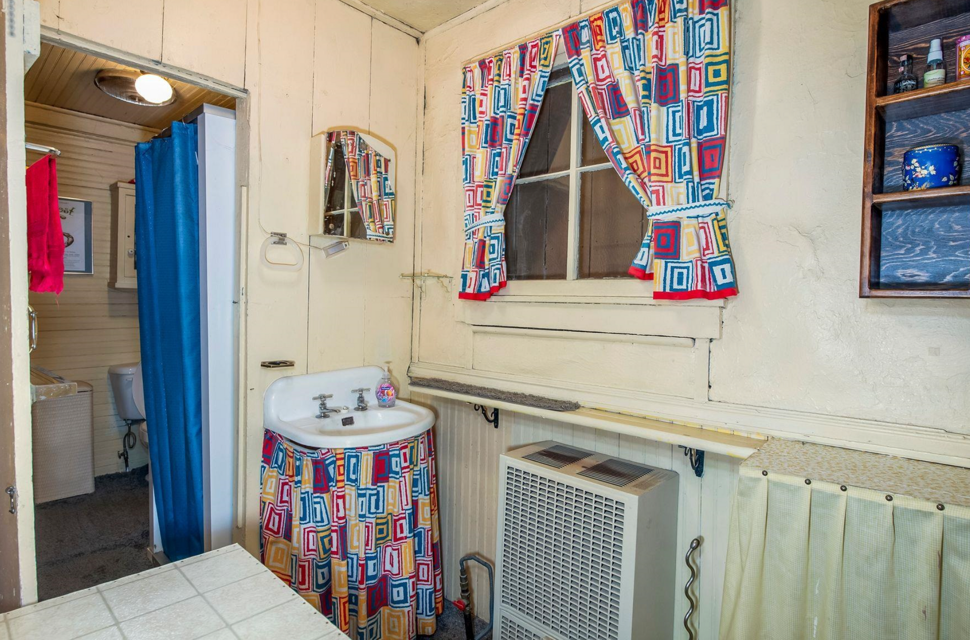 Small bathroom with colorful curtain, sink, mirror, radiator, and window.