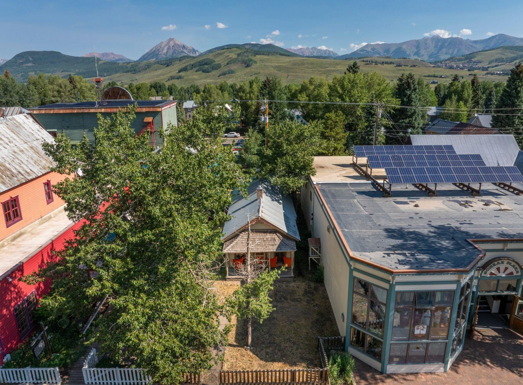Rural hillside buildings with solar panels, trees, and mountain peaks in the background