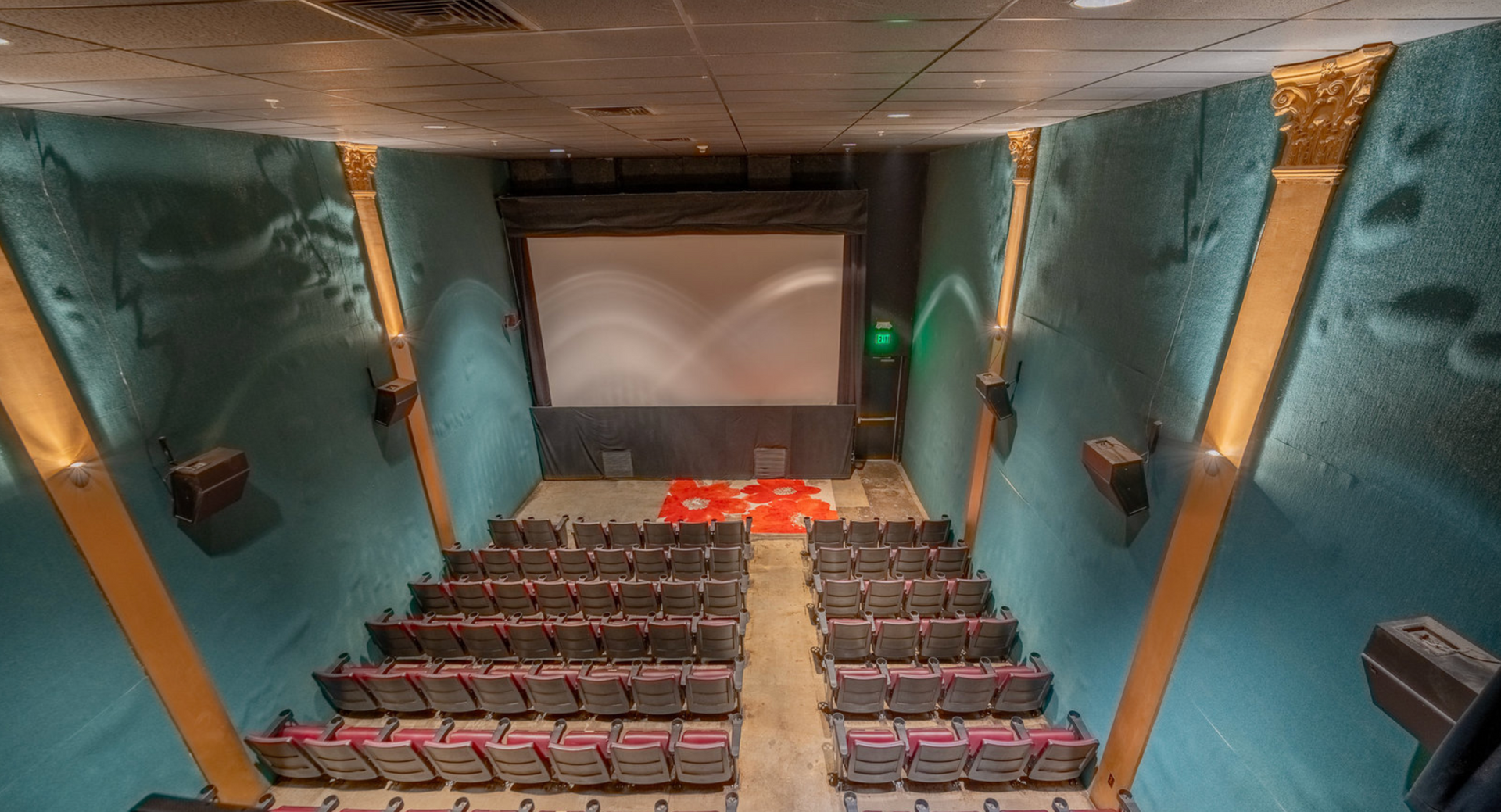 Empty theater auditorium with teal walls, red seats, and a large movie screen at the front