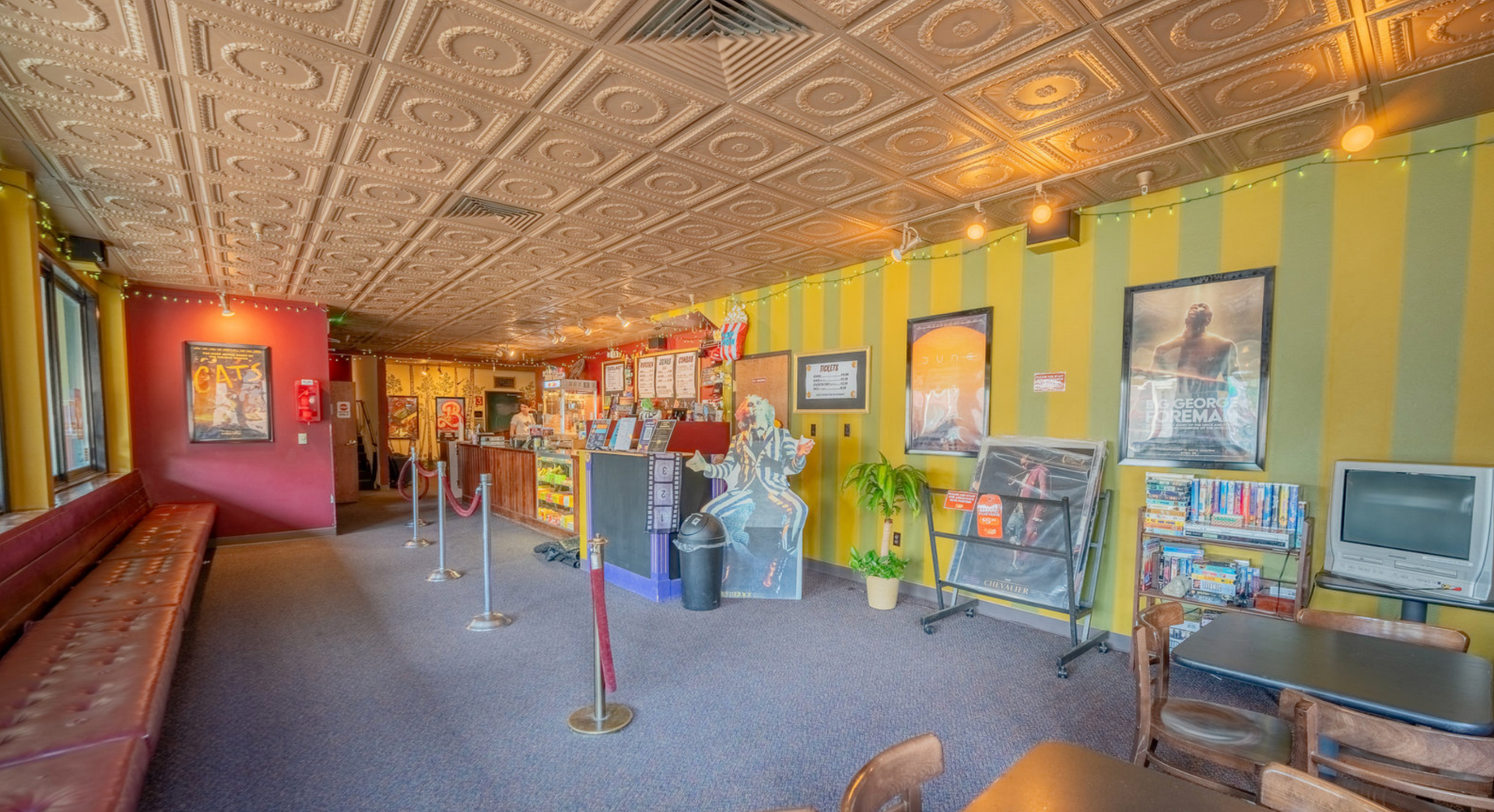 Vintage movie theater lobby with patterned ceiling, red walls, posters, display cases, and a ticket line