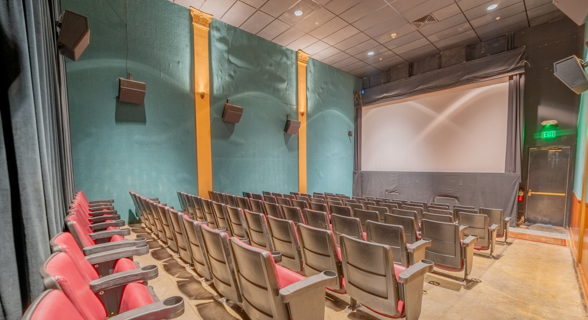Empty movie theater auditorium with red seats, teal walls, and a large projection screen.