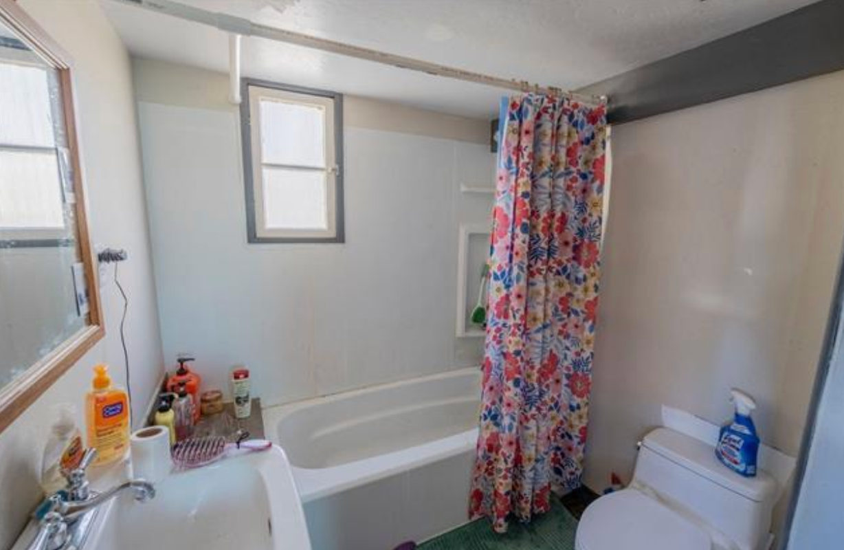Small bathroom with bathtub, colorful shower curtain, toilet, and sink on the left.
