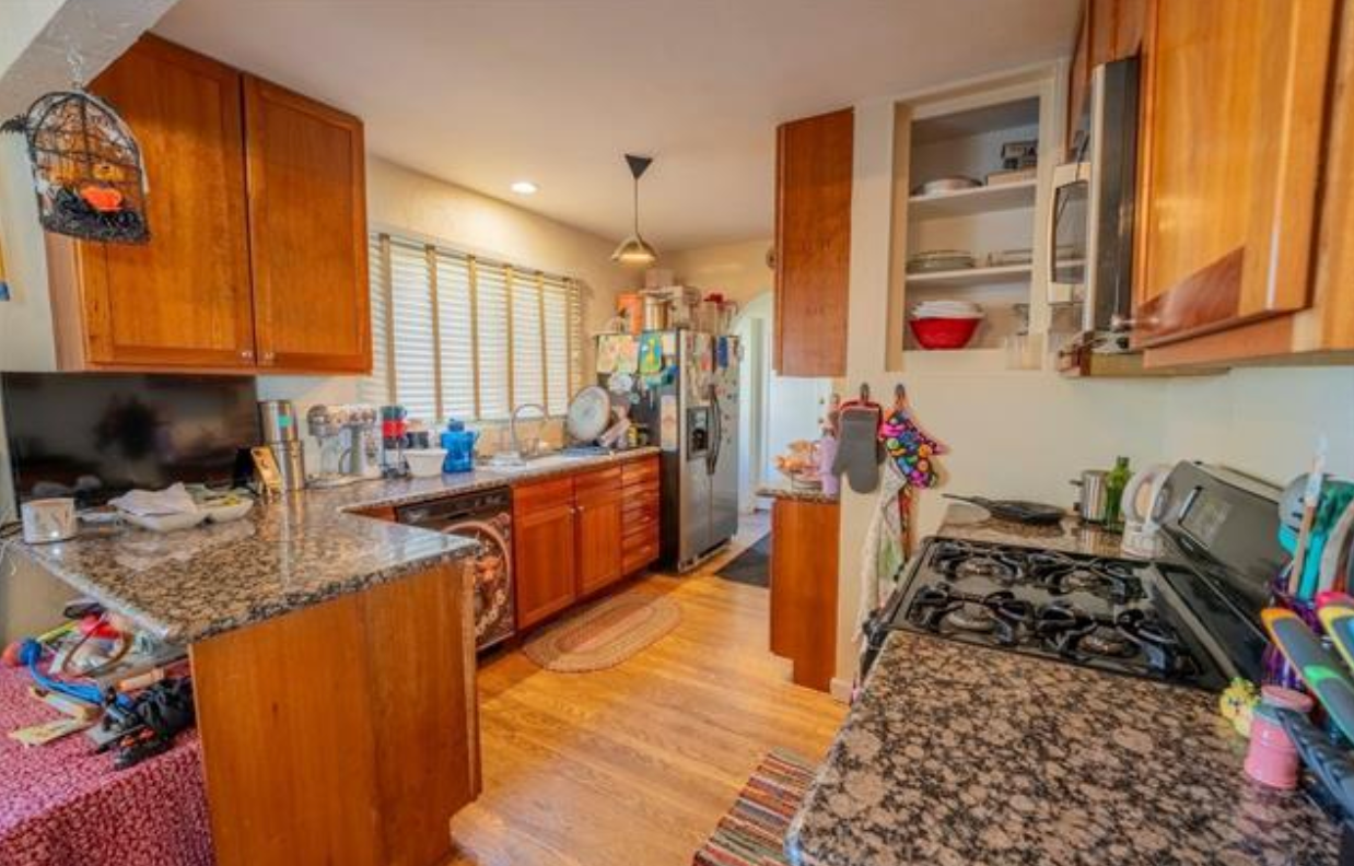 Bright kitchen with wooden cabinets, granite counters, gas stove, sink, and sunlight through the window.