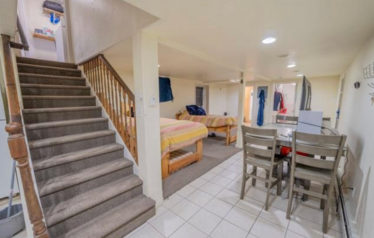 Basement room with carpeted stairs, bed, dining table, and tiled floor.