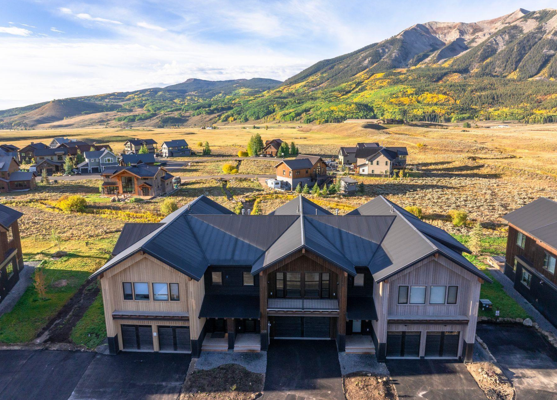 Modern house in a rocky mountain valley with scattered homes and yellow autumn hills under a clear sky