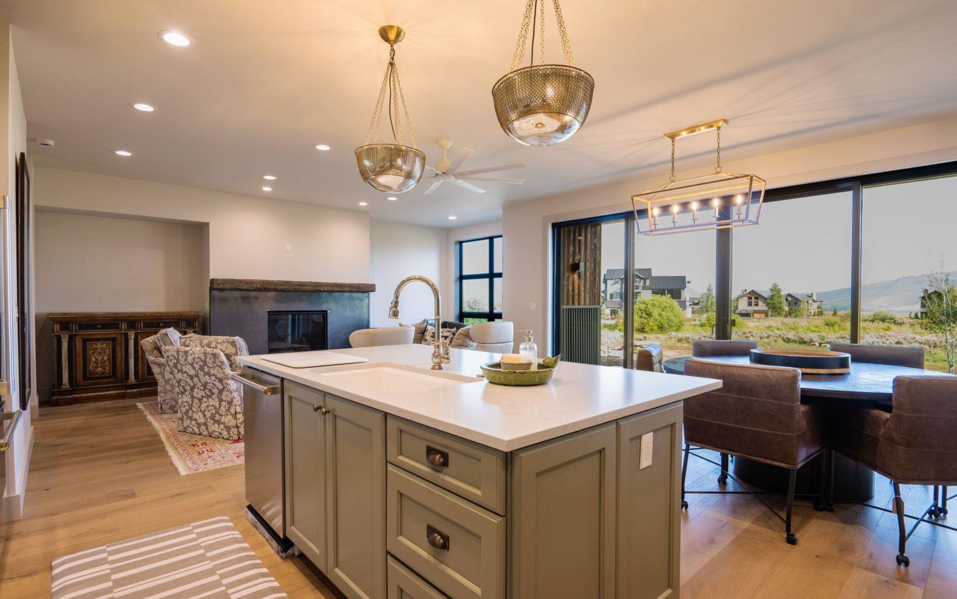 Bright modern kitchen with island, pendant lights, dining area, and large windows overlooking a patio