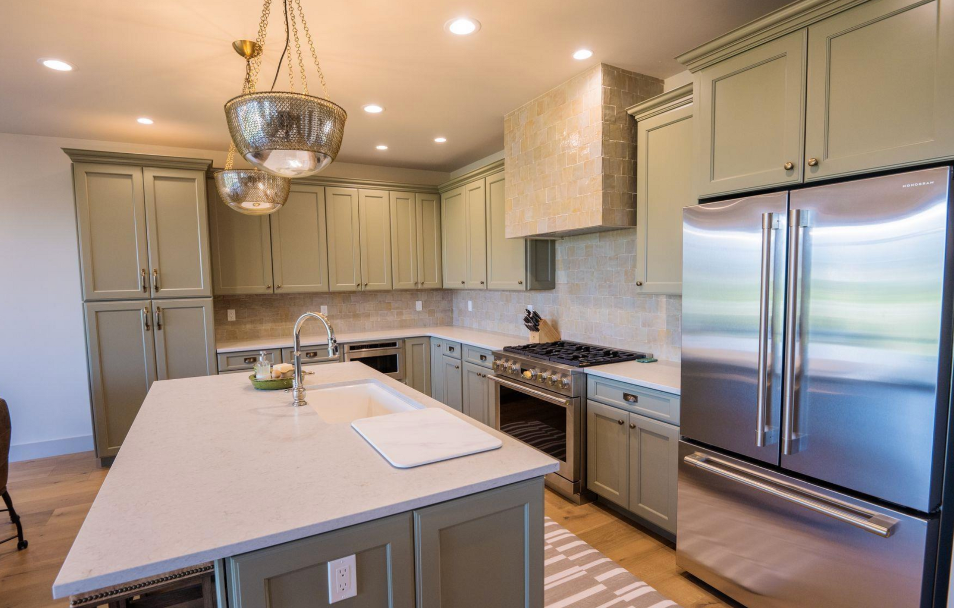 Modern kitchen with stainless steel appliances, light cabinets, and a large island under pendant lighting