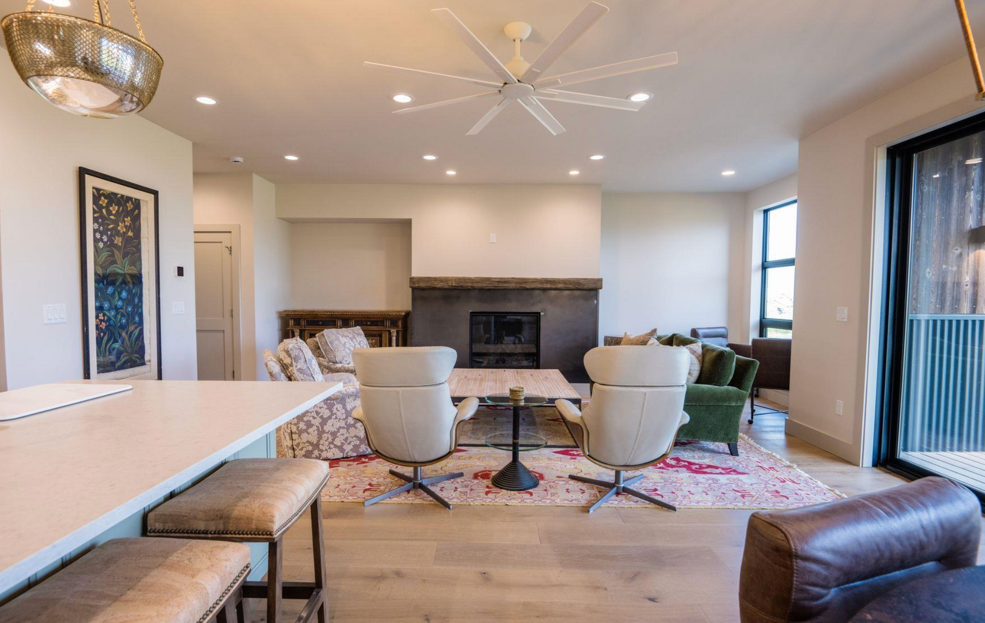 Modern living room with fireplace, two chairs, colorful rug, kitchen bar, and sliding glass door