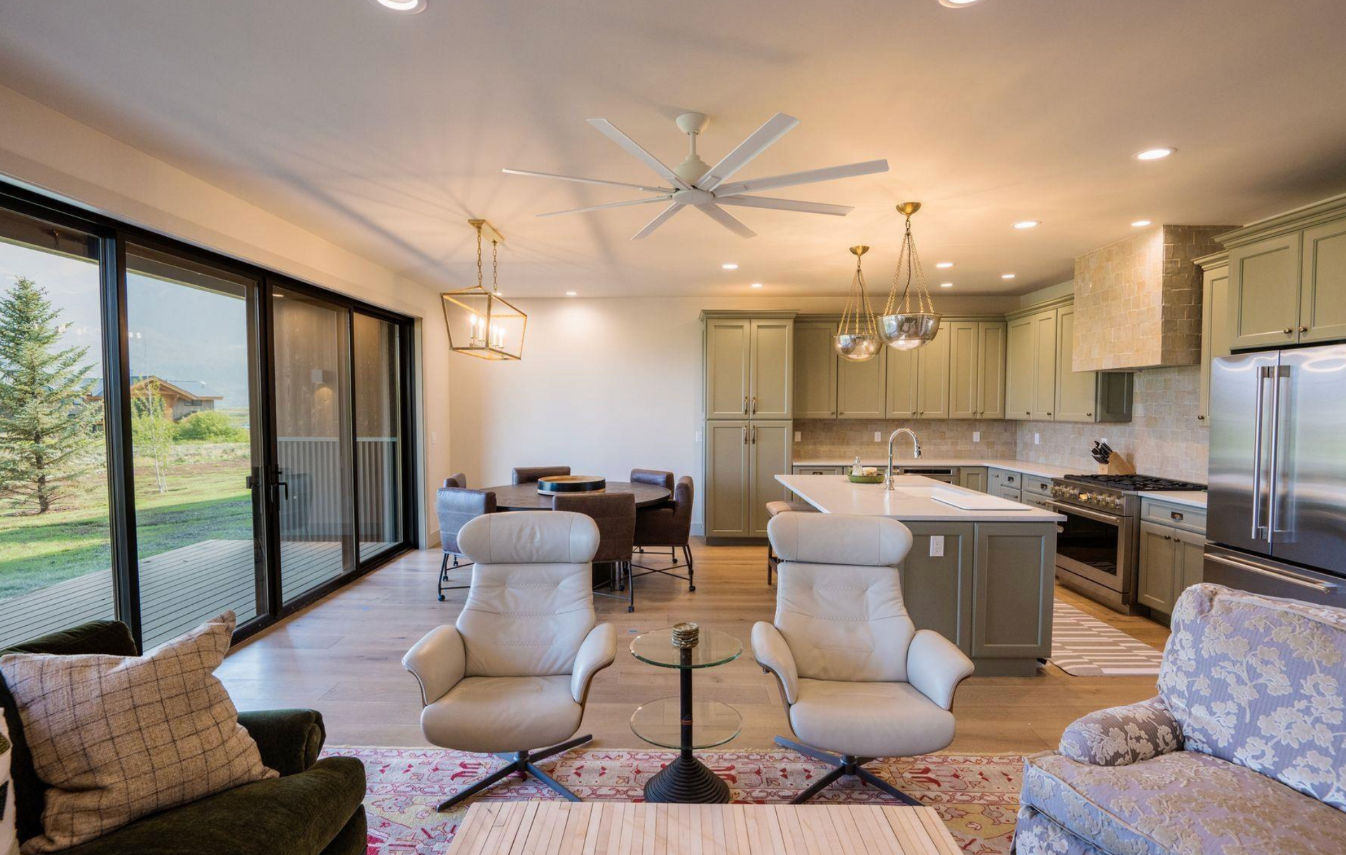 Modern open-plan living room and kitchen with large windows, neutral furniture, and island seating