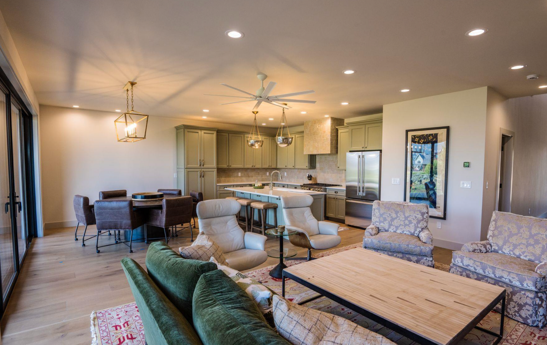 Open-plan living room and kitchen with green sofa, dining table, island, and light wood floors