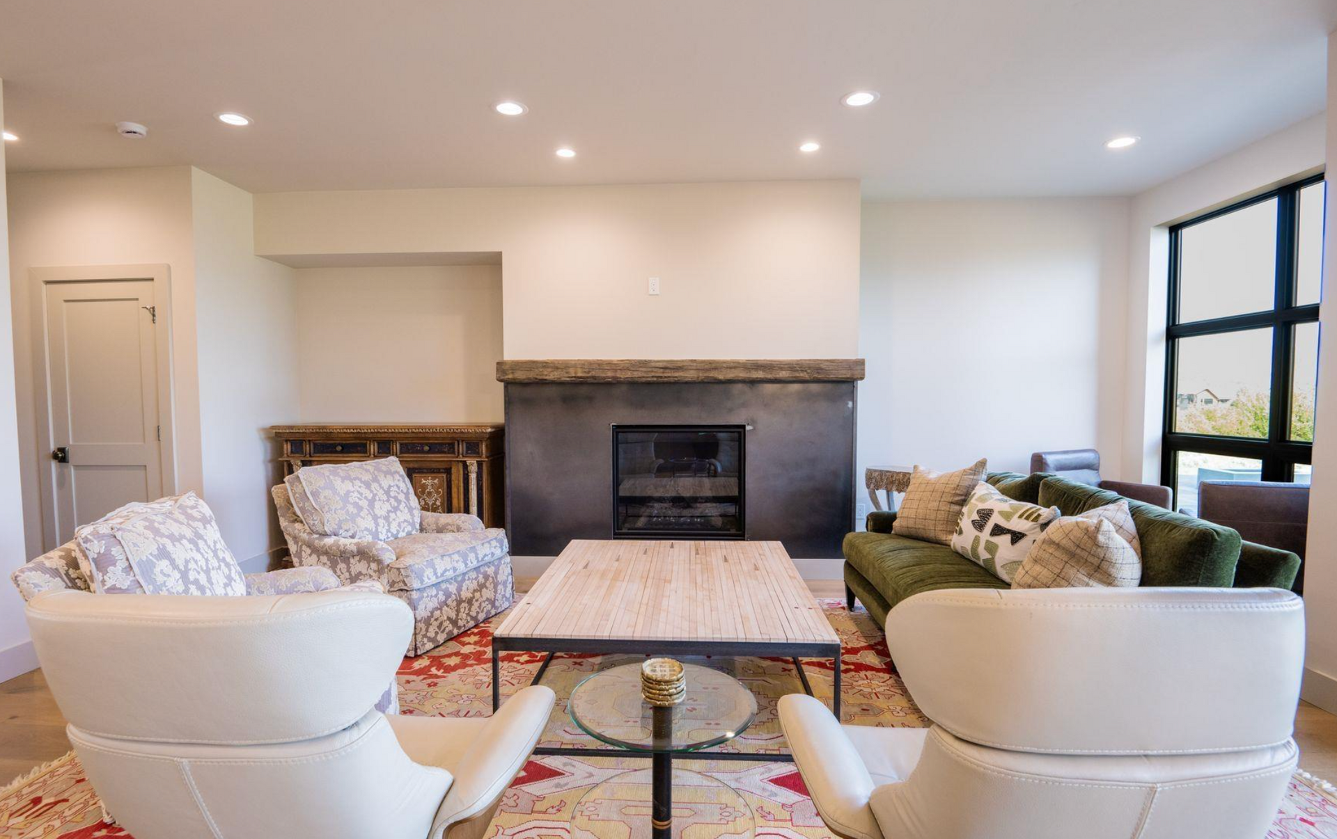 Bright living room with a fireplace, white chairs, sofas, and a coffee table near large windows.