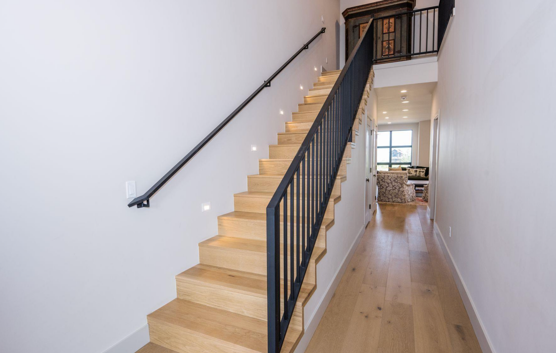 Narrow staircase with black railing in a bright home hallway leading to a room at the end
