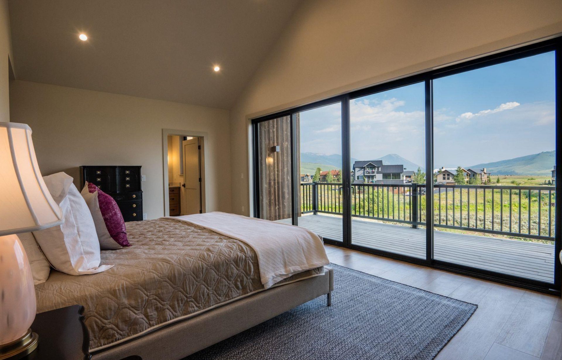 Modern bedroom with a bed, gray rug, and sliding glass doors opening to a mountain view.