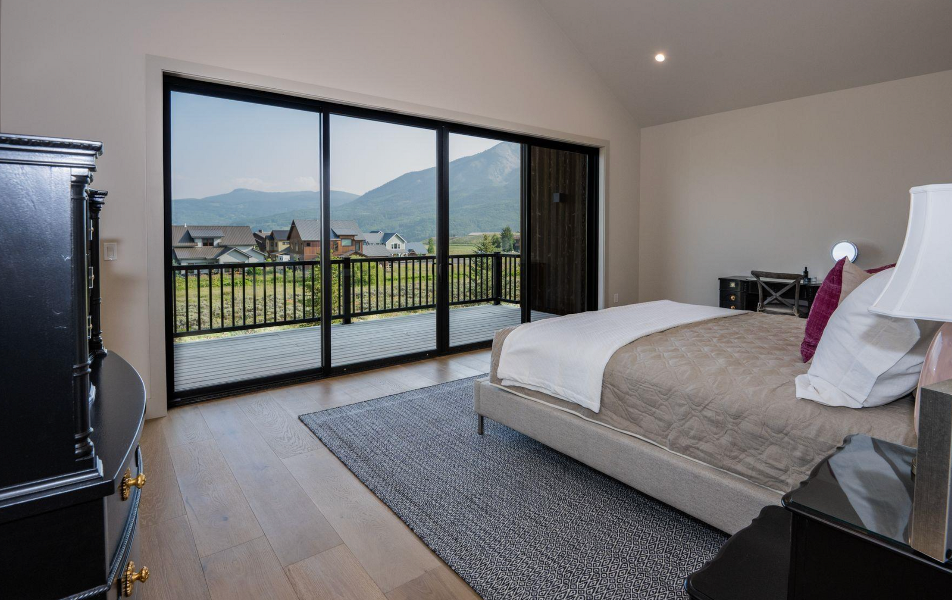 Modern bedroom with a bed, gray rug, and open sliding doors to a balcony with mountain views