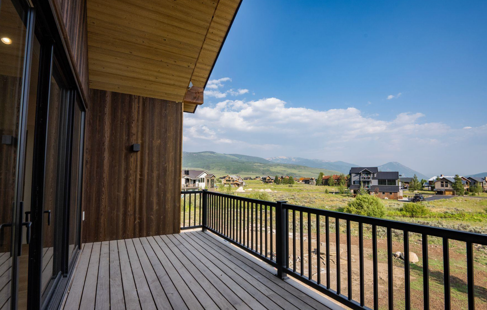 Covered wooden porch overlooking grassy fields and mountains under a blue sky