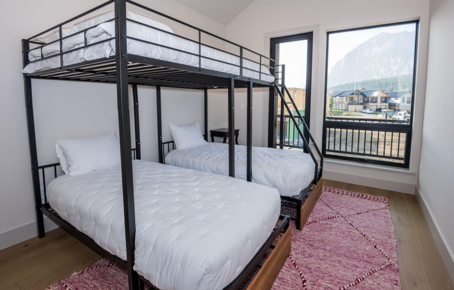 Twin metal bunk beds in a bright bedroom with pink rug and large windows overlooking a balcony