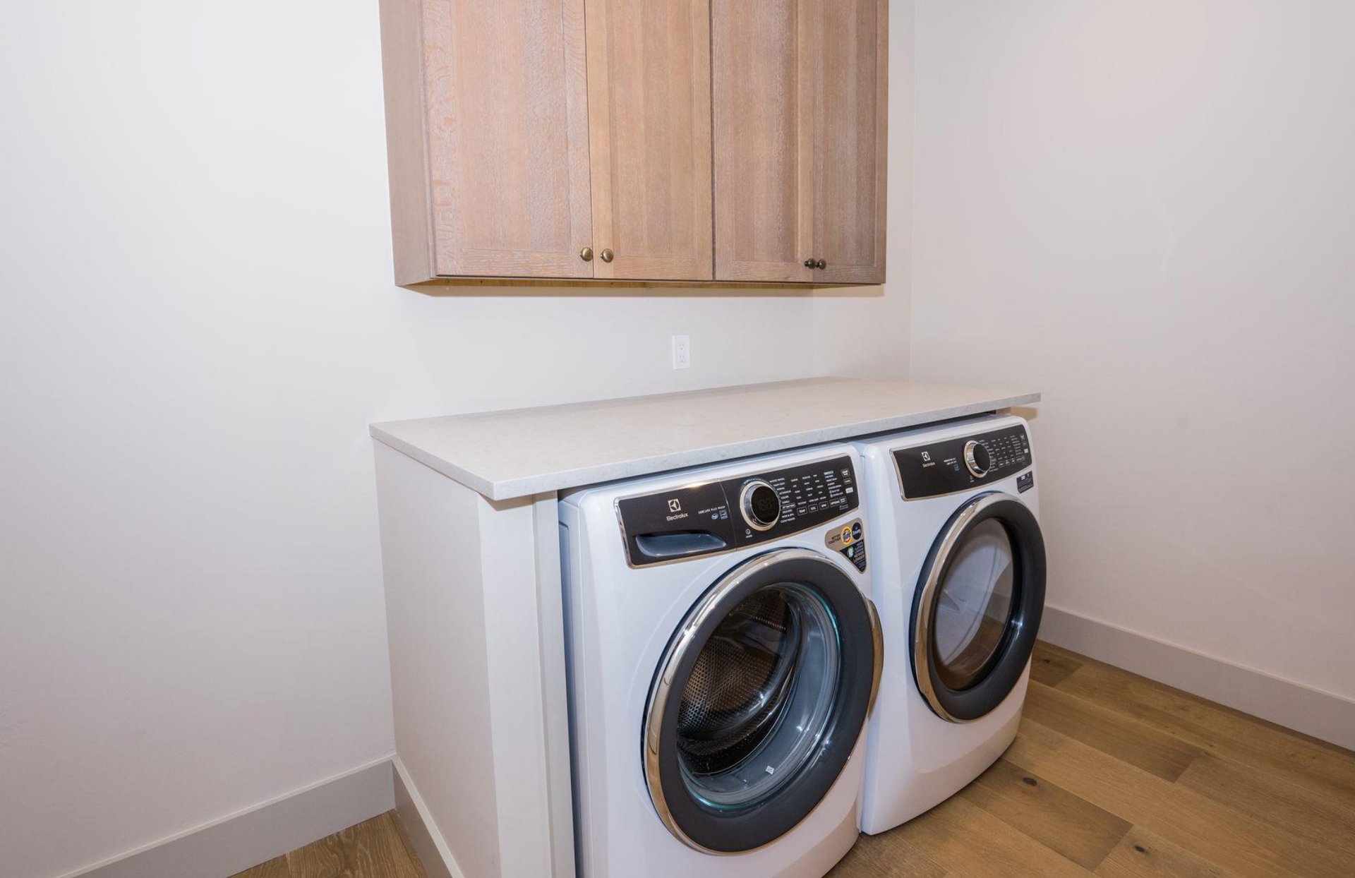 White front-loading washer and dryer in a small laundry nook with a wall cabinet above.
