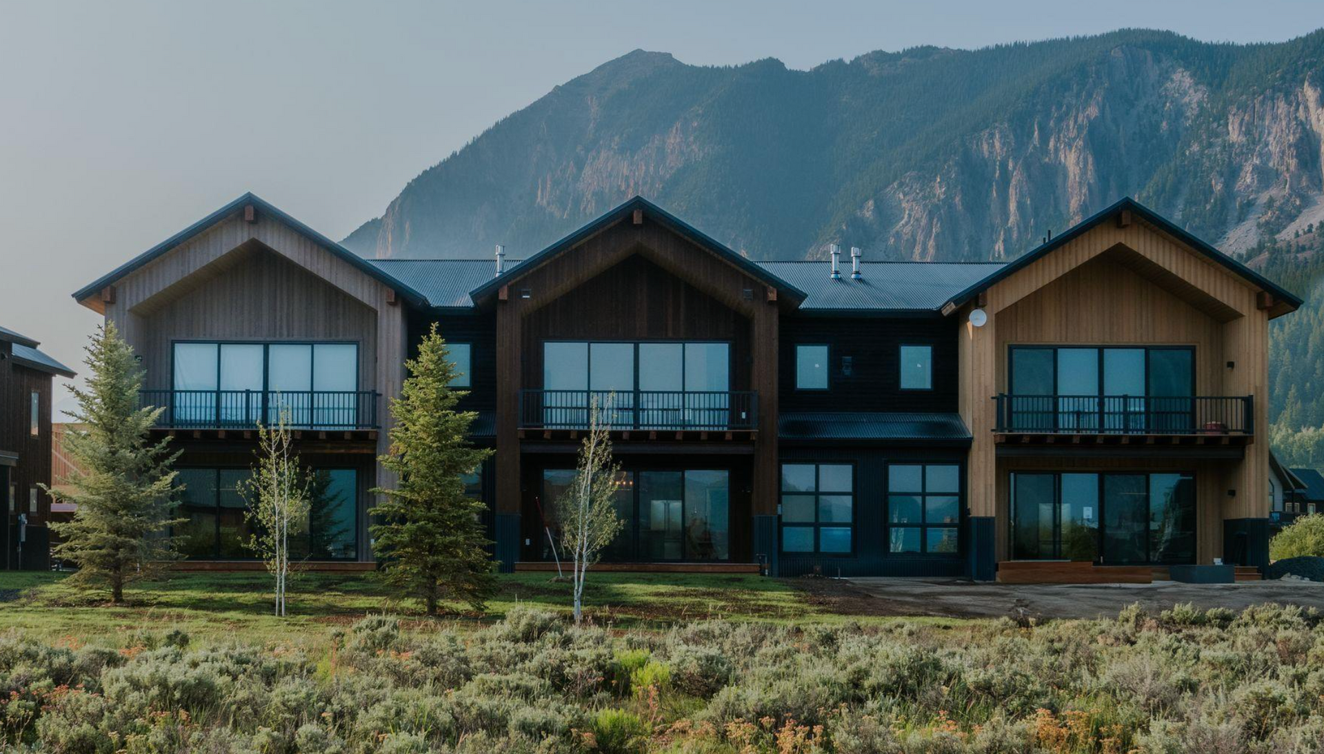 Modern lodge-style house with large windows in front of mountains and trees