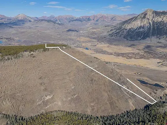 Aerial view of a dry hillside and valley with mountains in the background and a white route line across the slope