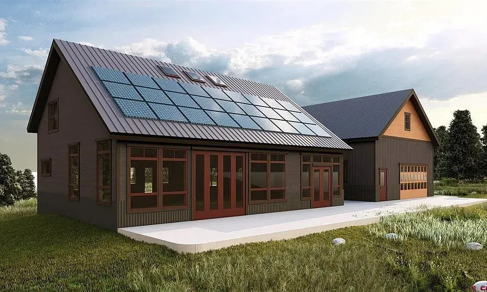 Modern house with solar panels, large windows, and a detached garage in a grassy yard